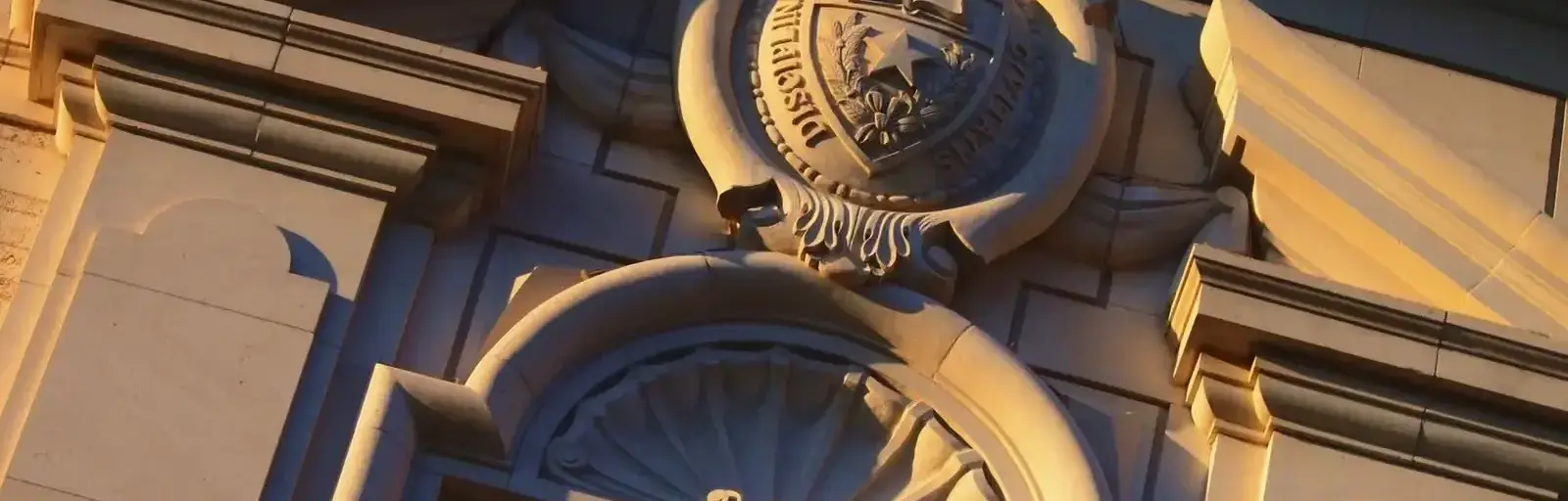 Close-up of a decorative stone facade featuring a circular crest above an arched opening, bathed in warm sunset light.